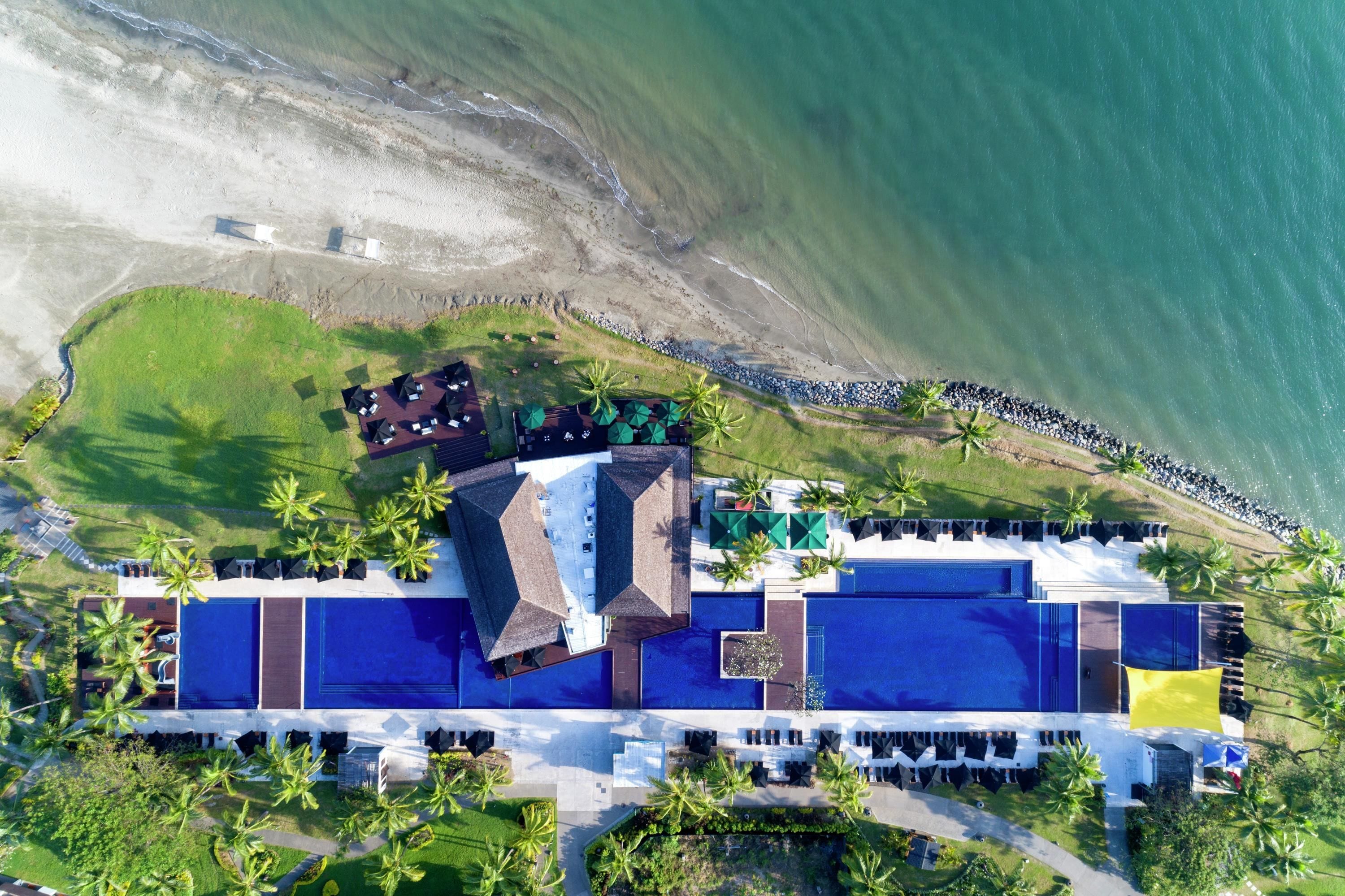 An aerial view of a resort with a pool area, beach access, and palm trees.