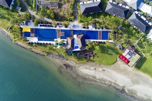 An aerial view of a resort with multiple swimming pools, a beach area, and lush greenery.