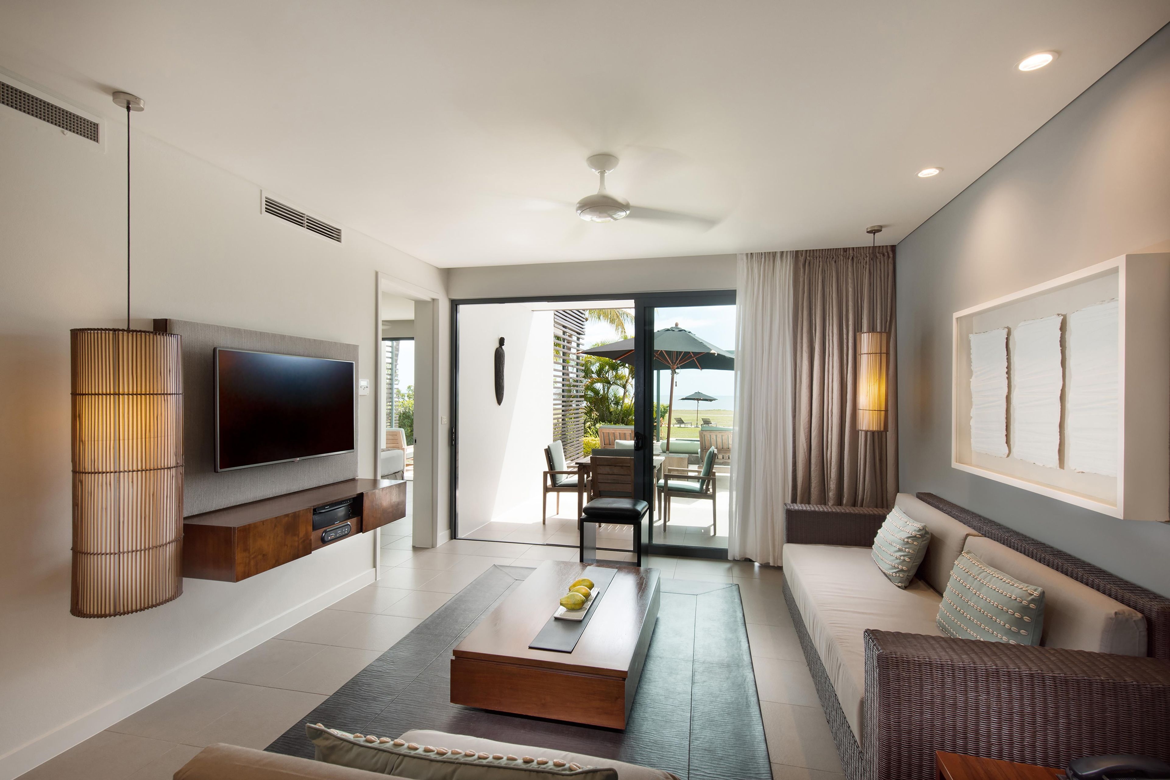 A modern living room with a flat-screen TV, a coffee table, a sofa, and a dining area with outdoor seating.