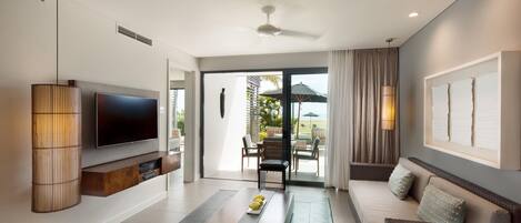 A modern living room with a flat-screen TV, a coffee table, a sofa, and a dining area with outdoor seating.