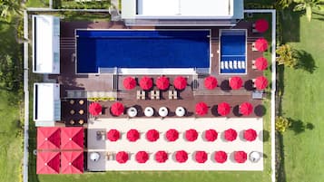 An aerial view of a resort with a swimming pool, multiple sun loungers, and umbrellas.