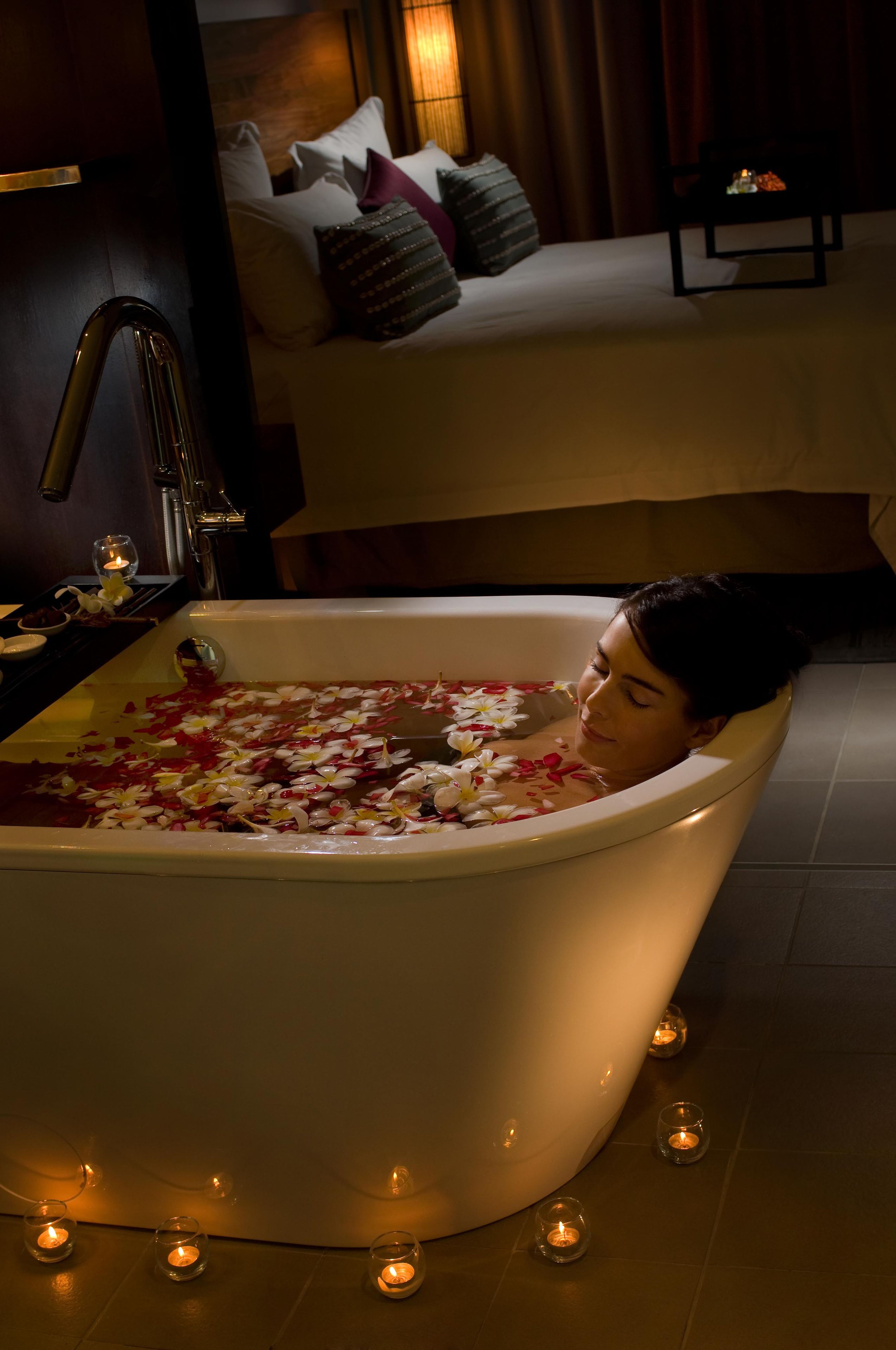 Una bañera llena de agua y pétalos de rosa, rodeada de velas.