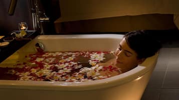 Una bañera llena de agua y pétalos de rosa, rodeada de velas.