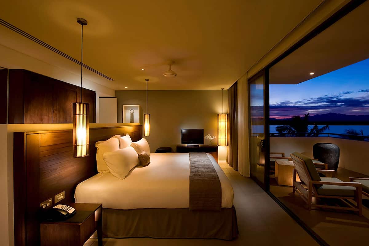 Ein modernes Hotelzimmer mit einem großen Bett, Nachttischlampen, einem Fernseher und Blick auf den Abendhimmel.