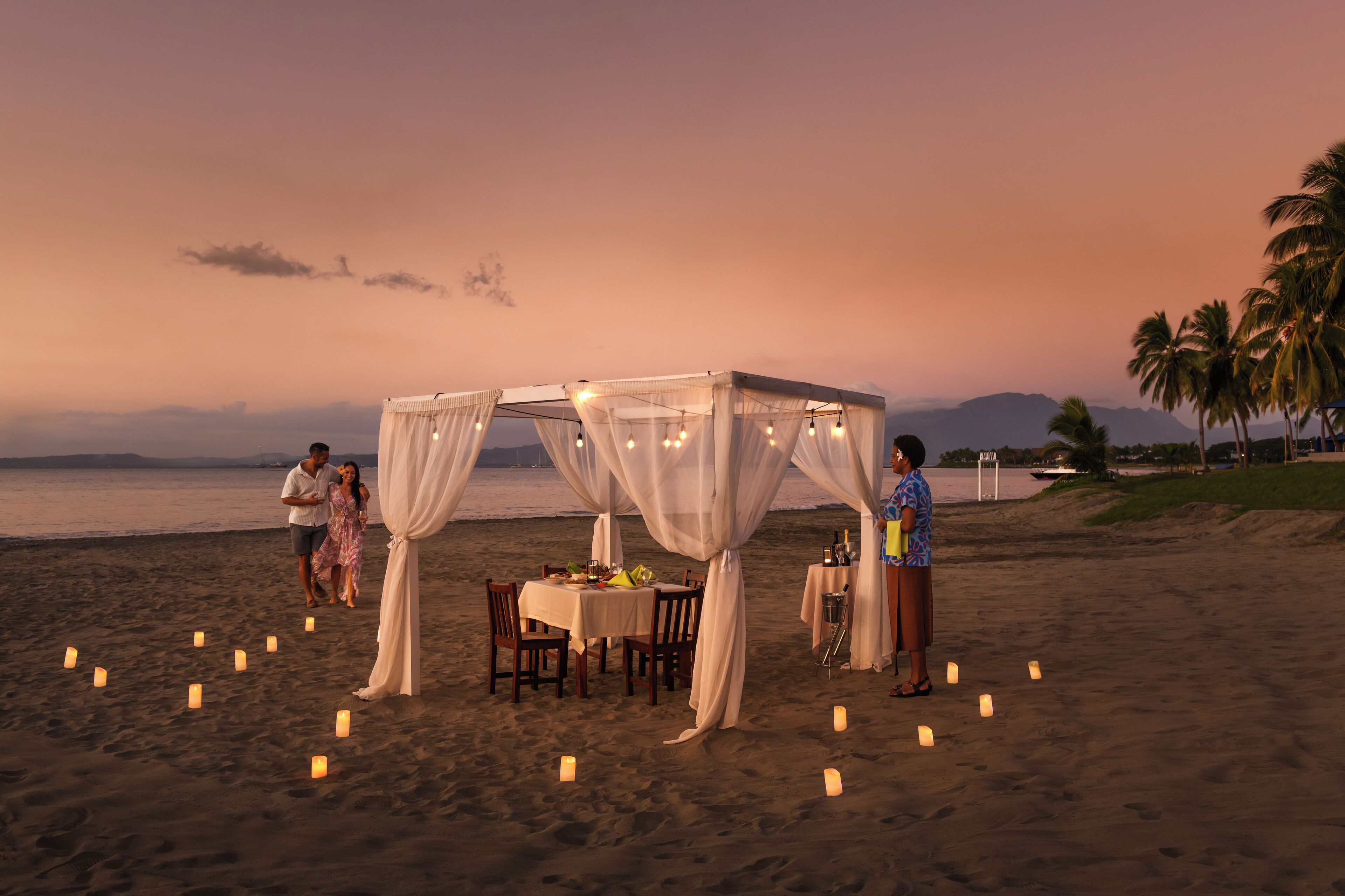 Un montaje para comer frente a la playa, con toldo, mesas, sillas y velas.