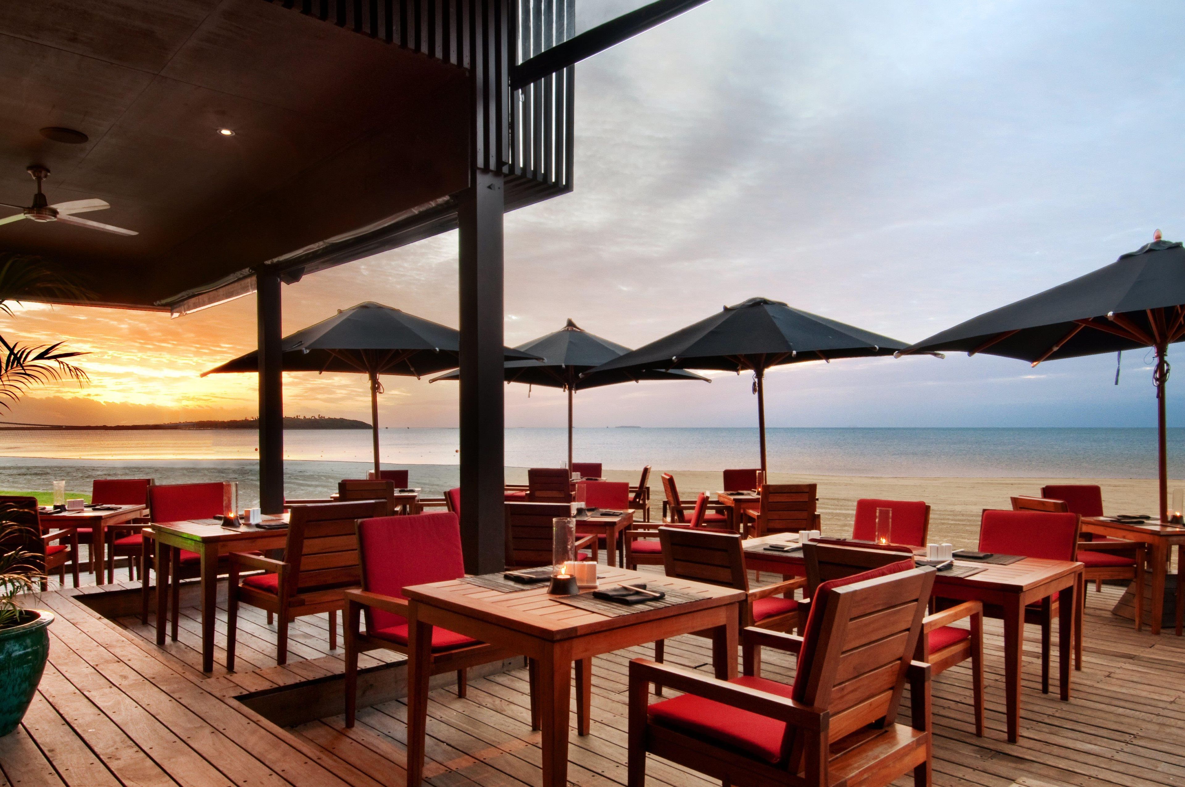 An outdoor seating area with tables and chairs, umbrellas, and a view of the sea.