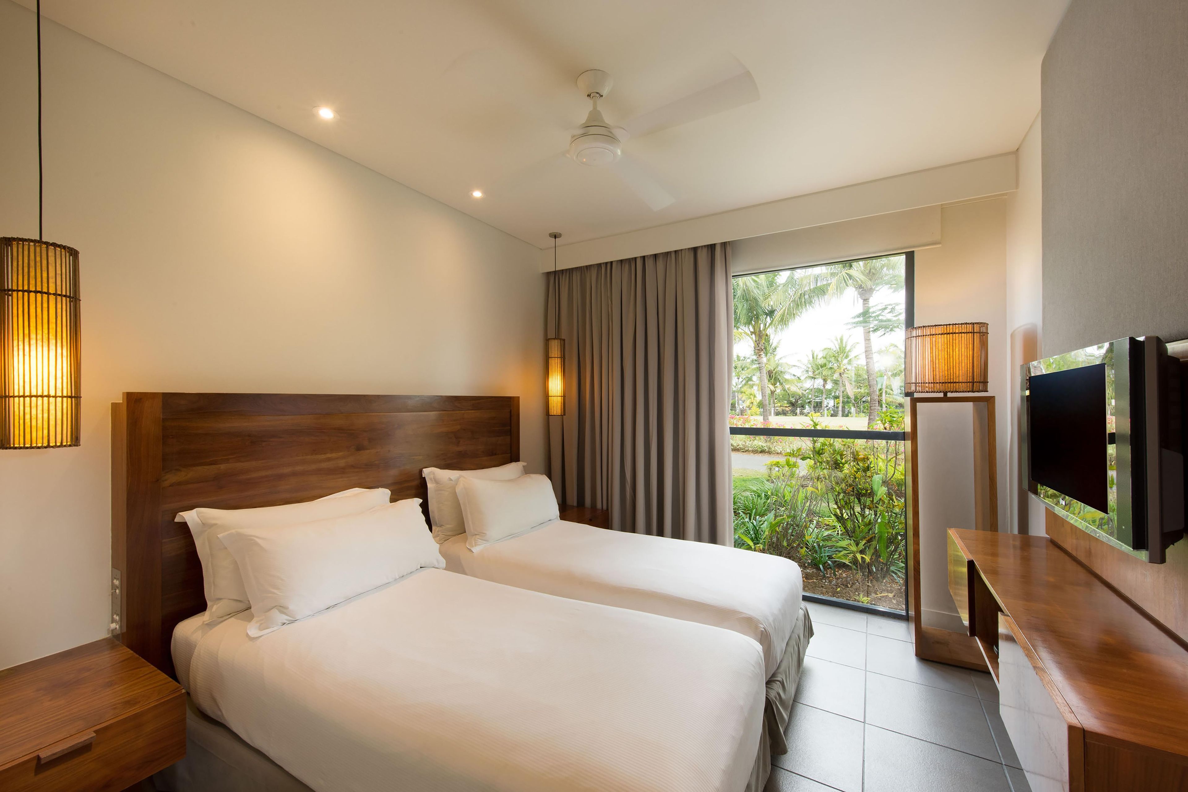 Habitación de hotel con dos camas, ventilador de techo, televisión y vistas al exterior.
