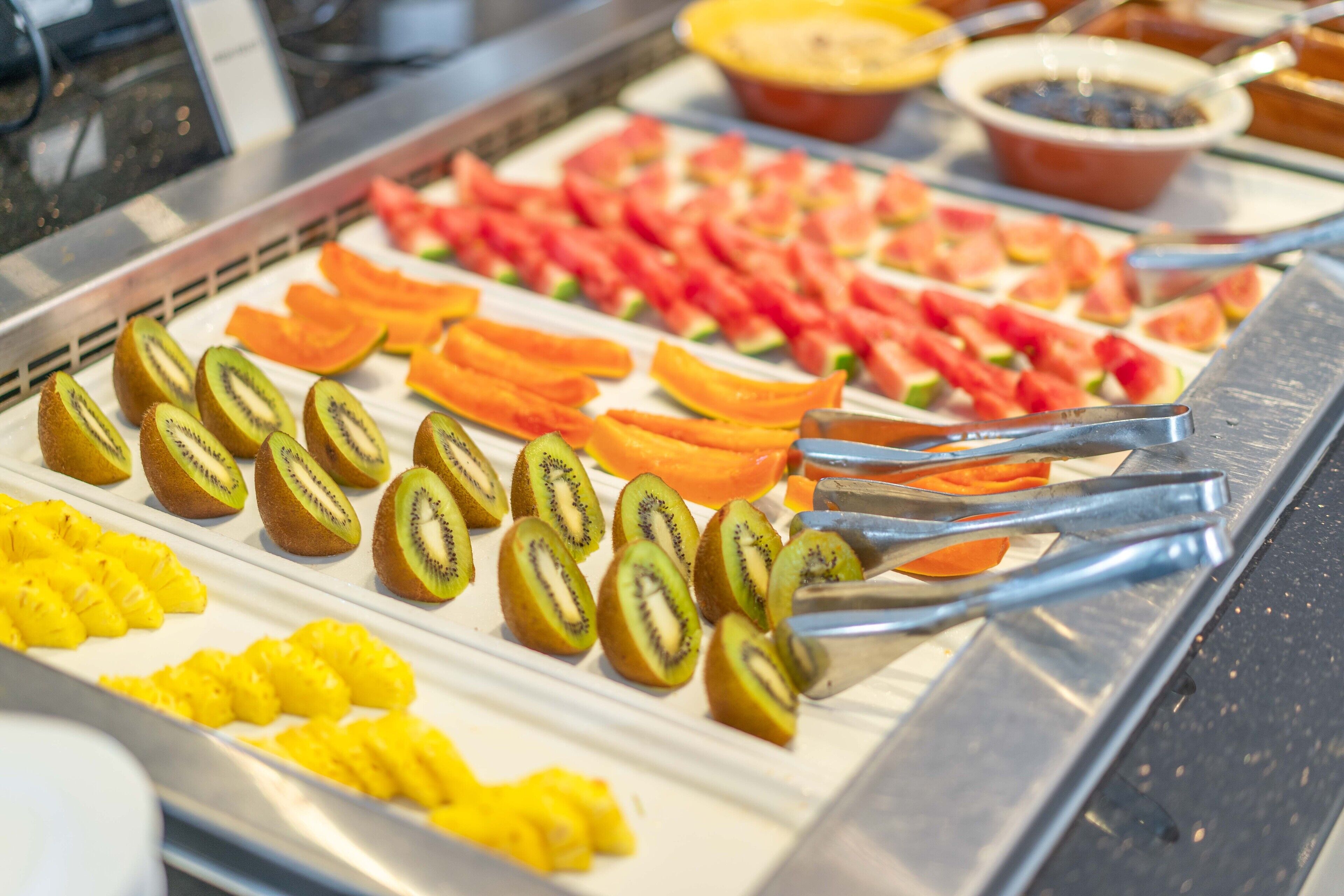A buffet with sliced fruits and vegetables, including kiwi, pineapple, and tomatoes.