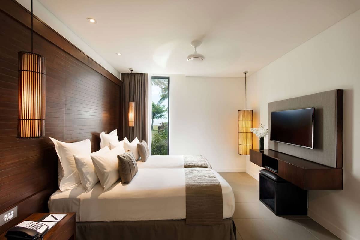Ein modernes Hotelzimmer mit einem großen Bett, einem an der Wand montierten Fernseher und einem Fenster mit Blick auf Grünflächen.