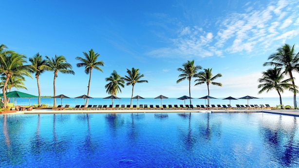 A pool with lounge chairs and umbrellas, palm trees, and a clear sky. - Hilton Fiji Beach Resort and Spa (Nadi)