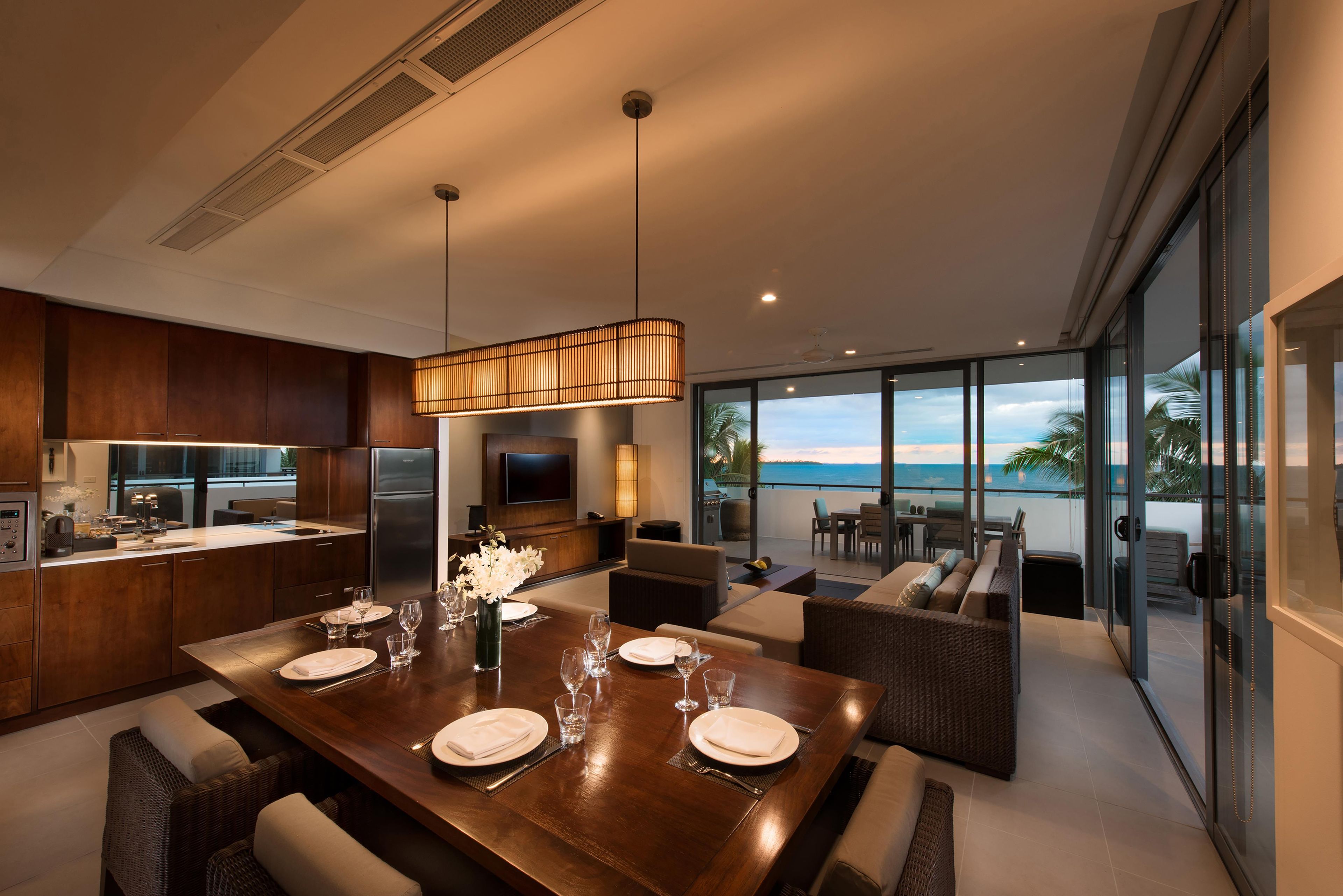 A modern kitchen with a dining area, a large TV, and a view of the ocean.