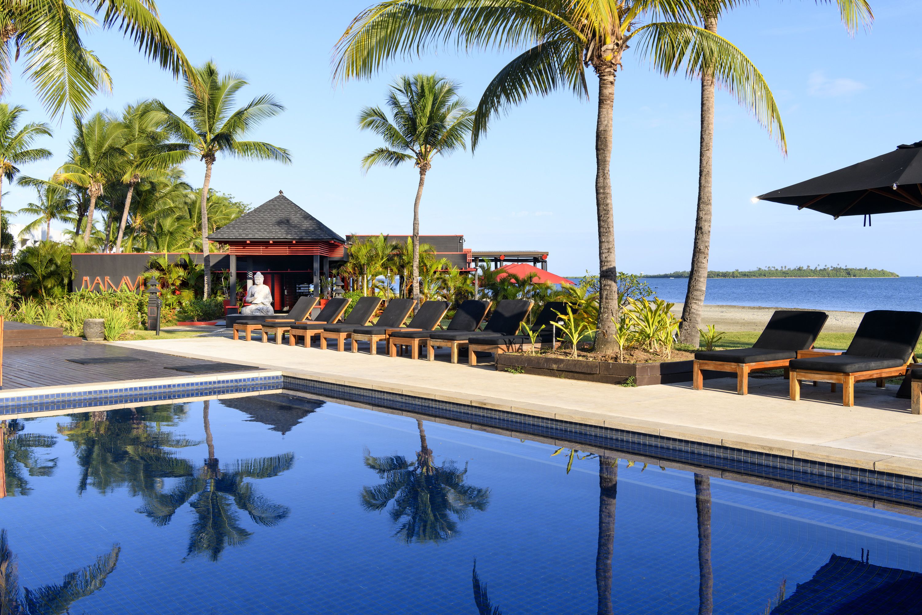 A poolside area with lounge chairs, palm trees, and a view of the ocean.