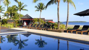 A poolside area with lounge chairs, palm trees, and a view of the ocean.