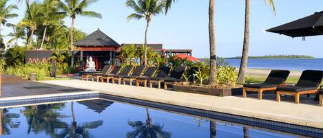 A poolside area with lounge chairs, palm trees, and a view of the ocean.