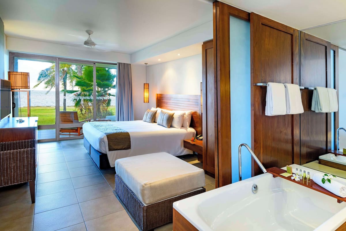 Ein Hotelzimmer mit einem großen Bett, einer separaten Sitzecke, einem Schreibtisch, einer Badewanne und Meerblick.