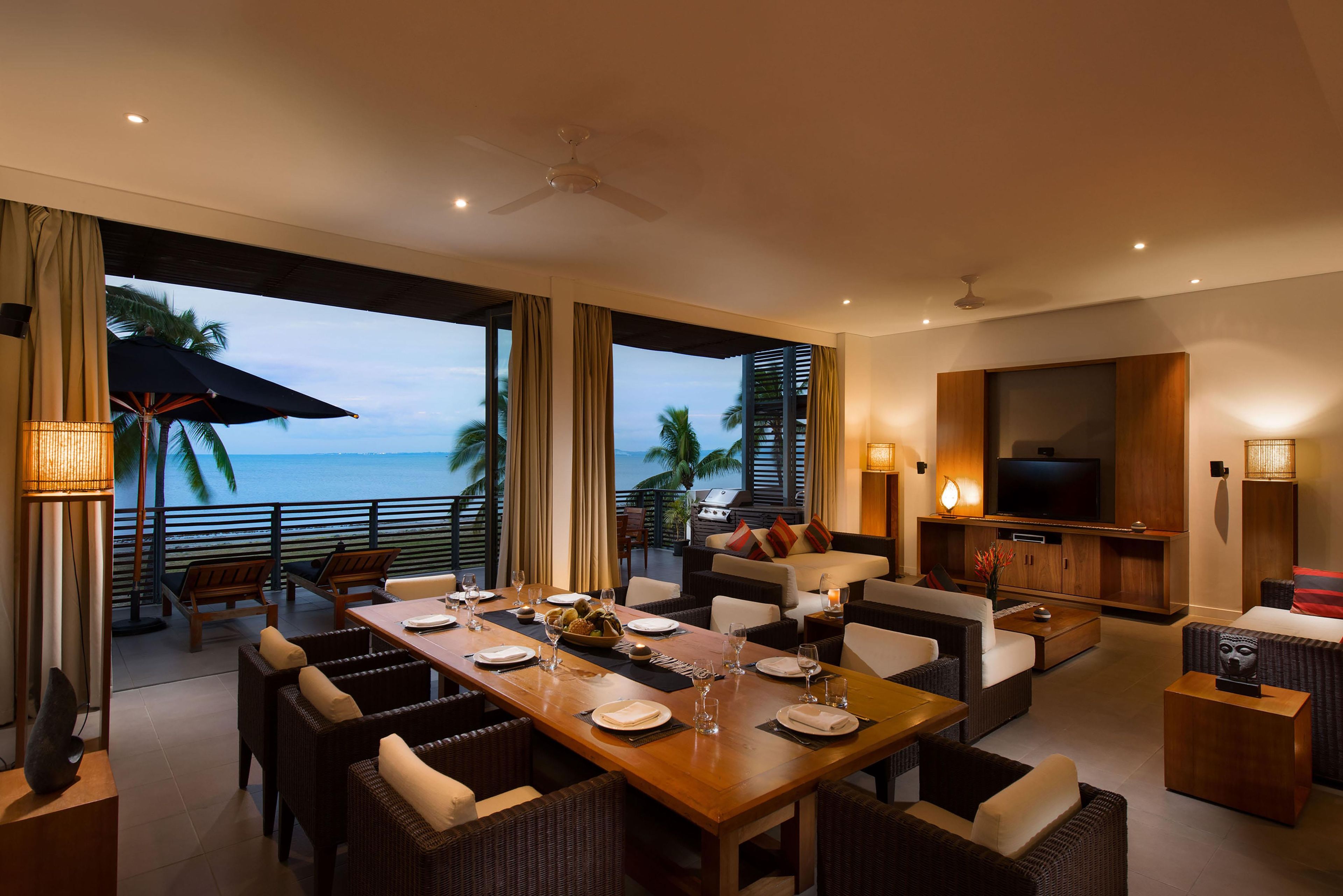 Un moderno comedor con vista al mar, amoblado con sillas de mimbre y una mesa de madera dispuesta para comer.
