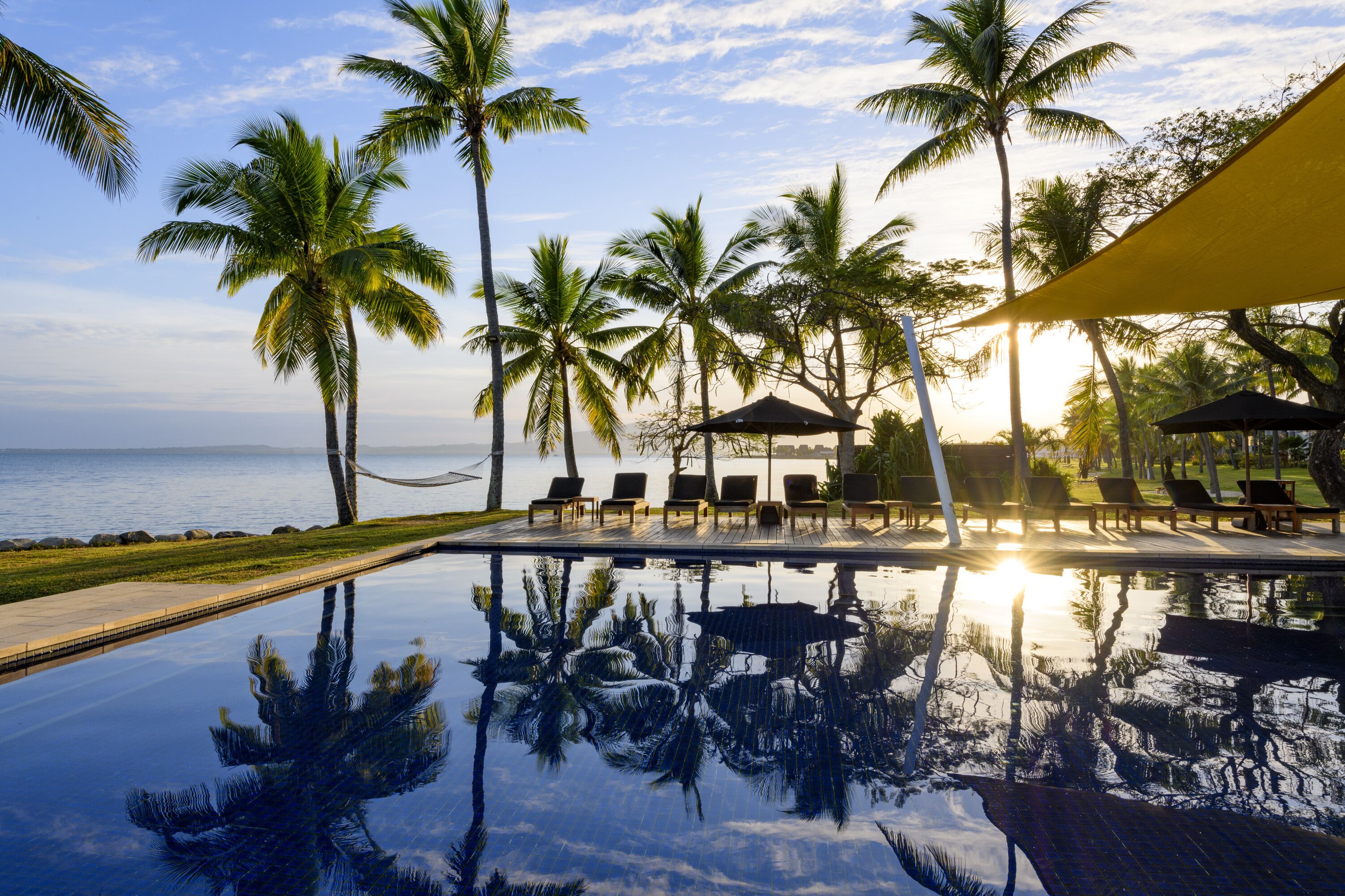 A poolside area with lounge chairs, palm trees, and a view of the ocean.
