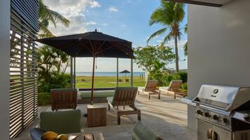 A patio with outdoor furniture, a grill, and a view of the ocean.