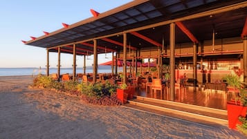 A beachfront restaurant with outdoor seating, a bar, and a view of the ocean.