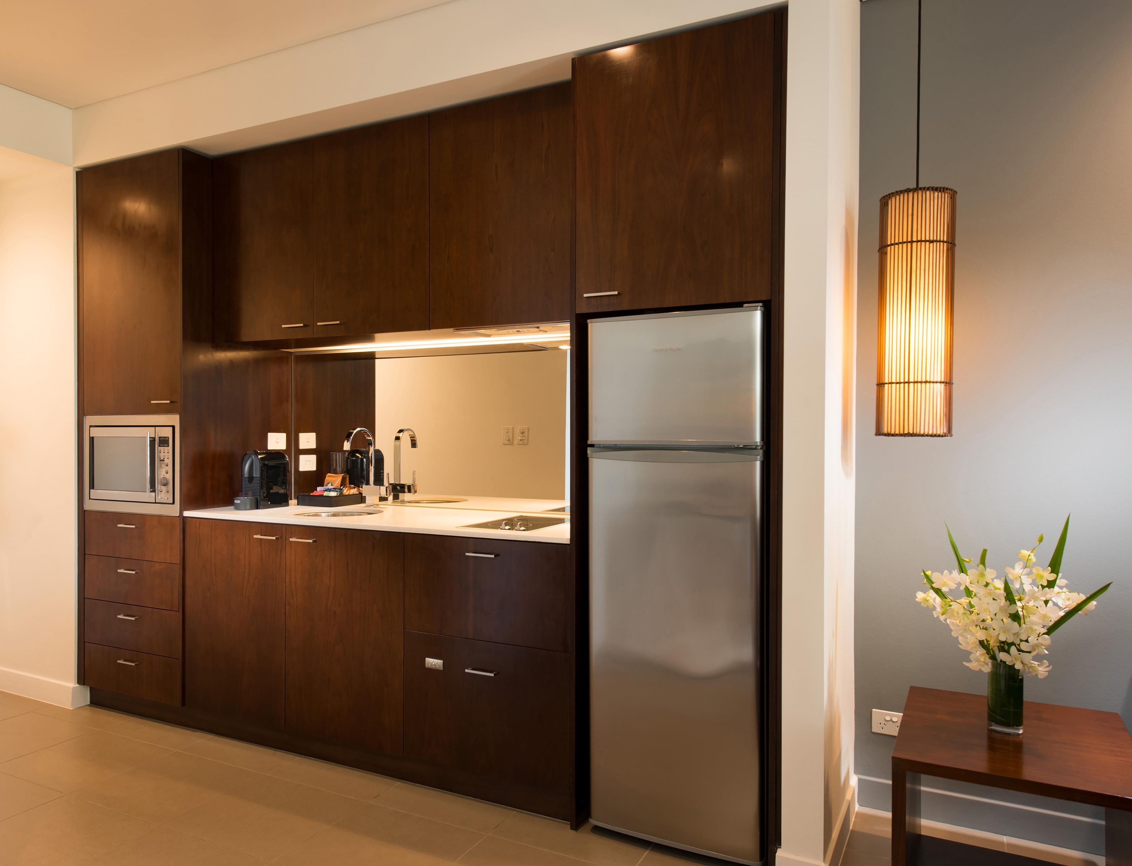 A modern kitchen with dark wooden cabinets, a stainless steel refrigerator, a microwave, and a coffee maker.