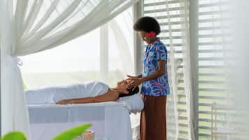 A person receiving a massage in a room with a large window, a white bed, and a small table with a bowl and water bottles.