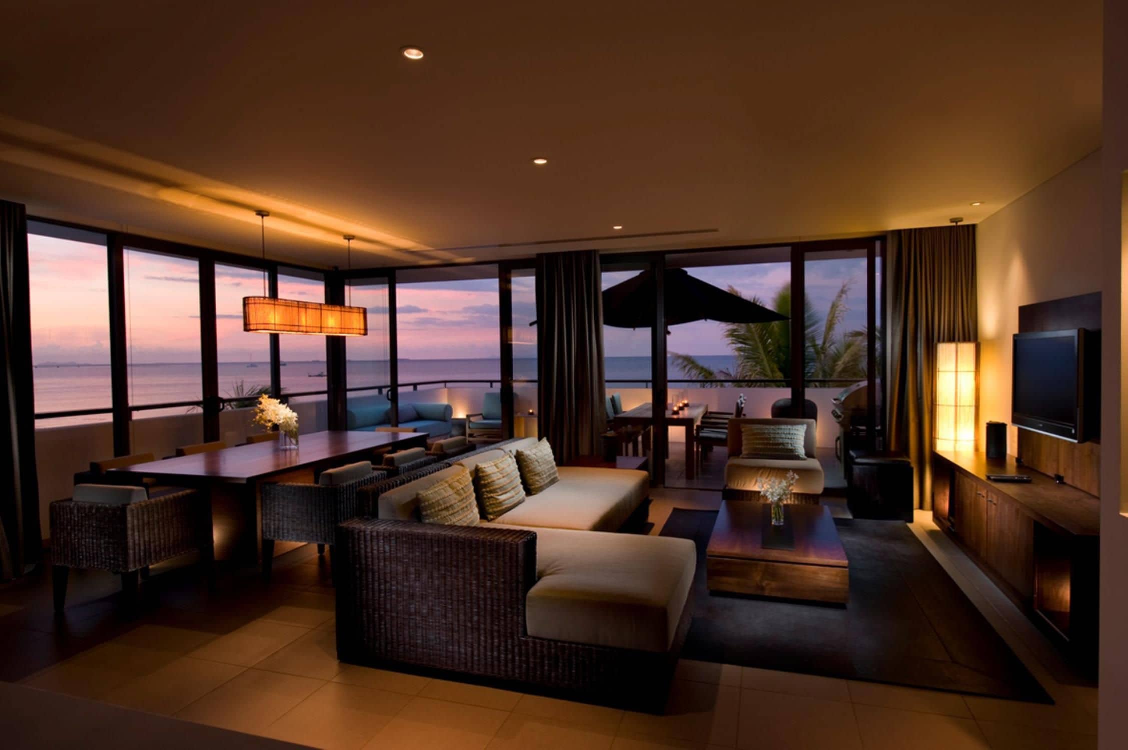A modern living room with a large window overlooking the sea, furnished with sofas, a coffee table, and a TV.