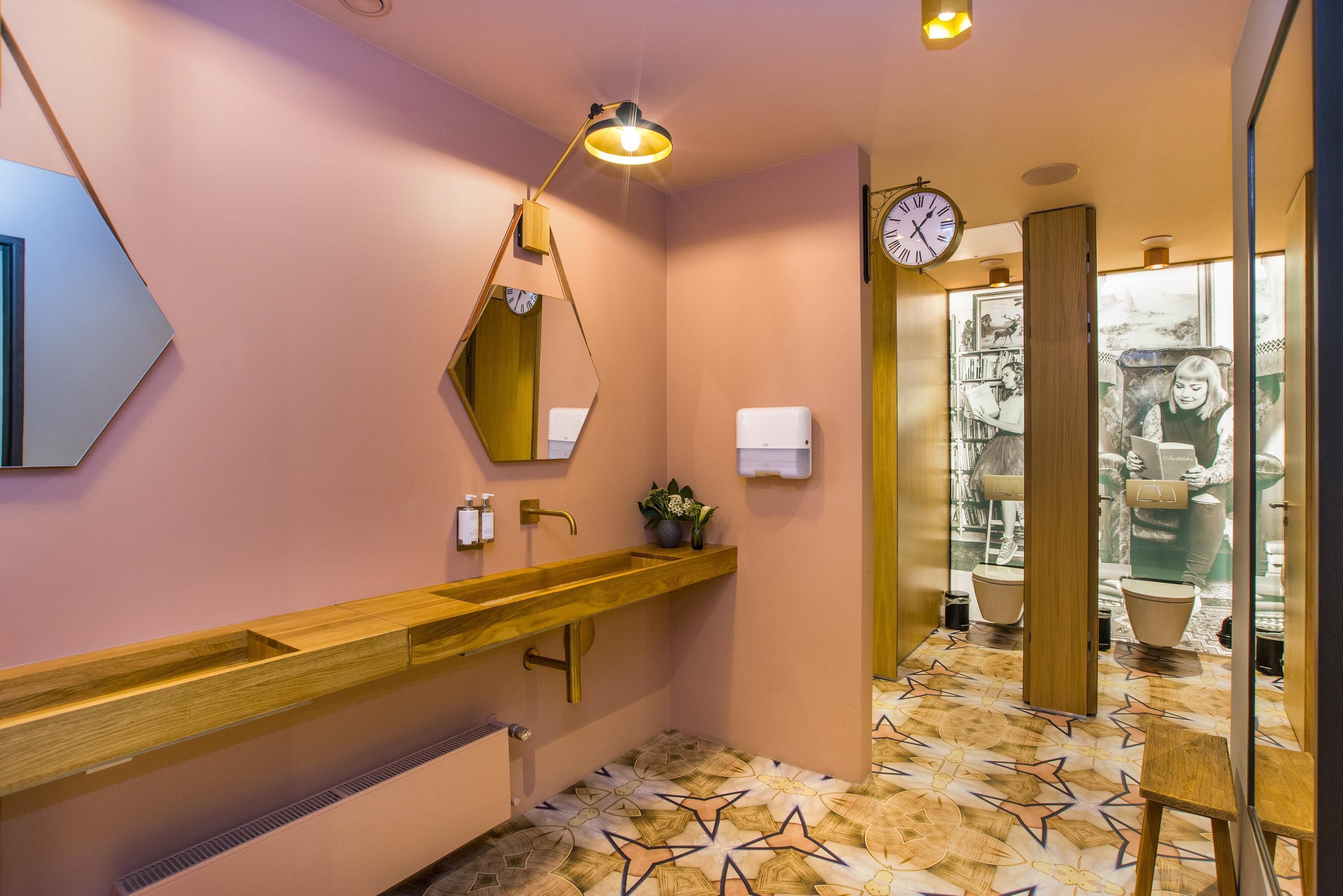 A modern bathroom with a wooden vanity, a mirror, a wall clock, and a patterned floor.