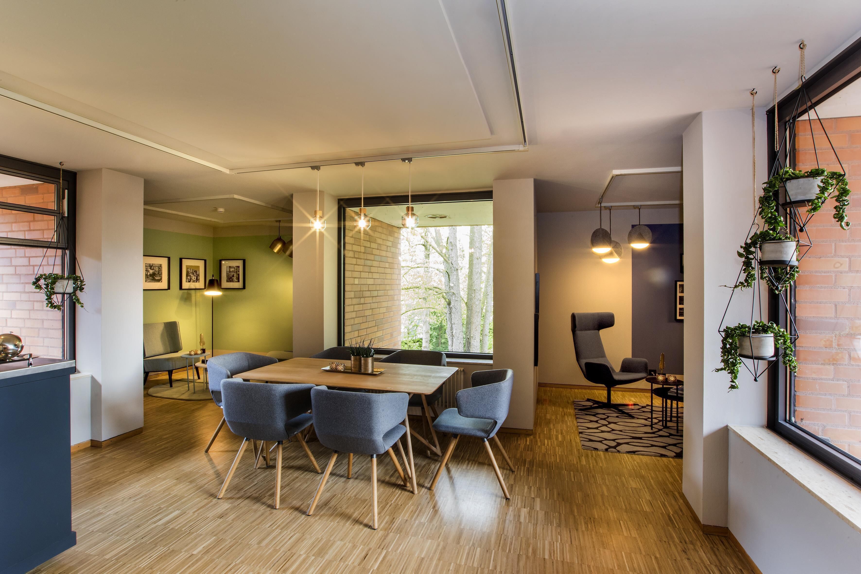 Un espace de salle à manger moderne avec une table en bois, des chaises grises, des luminaires suspendus et un mur en briques.
