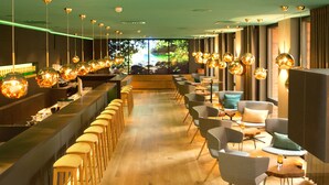 A restaurant interior with a long counter, multiple seating areas, and hanging spherical light fixtures. - Arcadeon (Hagen)