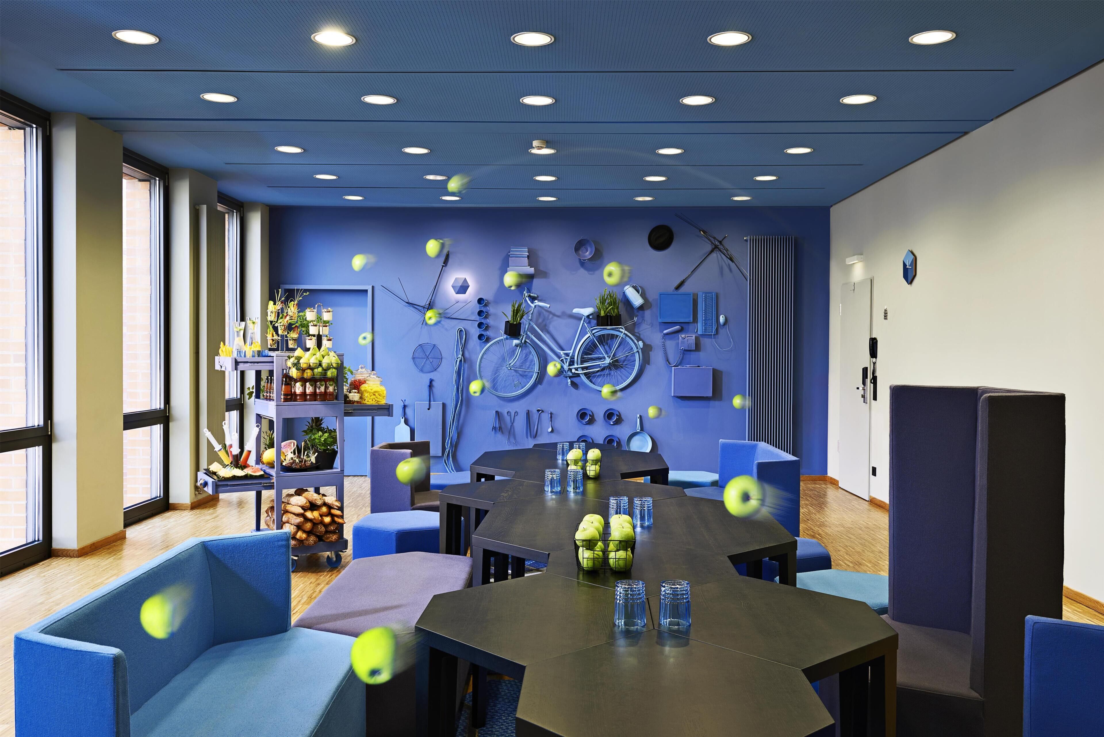 Una sala conferenze moderna con un lungo tavolo, sedie blu e un'opera d'arte a tema bicicletta.