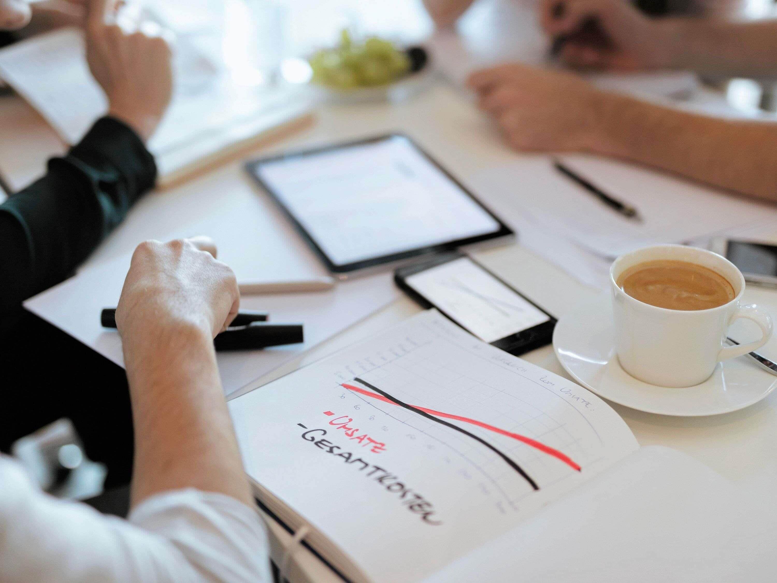 Een vergadering met documenten, een tablet en een kop koffie op een tafel.