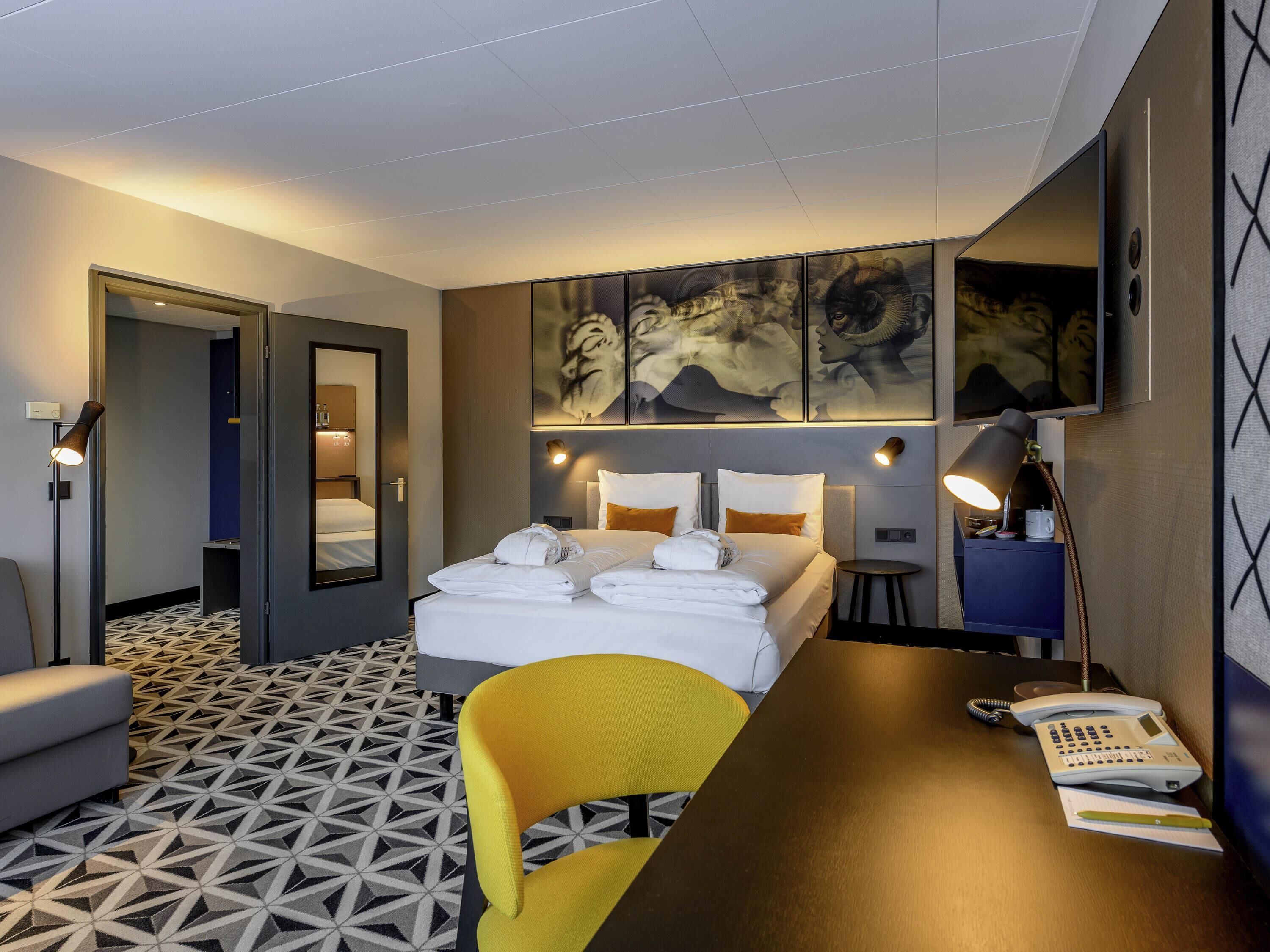 A hotel room with a bed, bedside tables, a desk with a telephone, a chair, and a patterned floor.