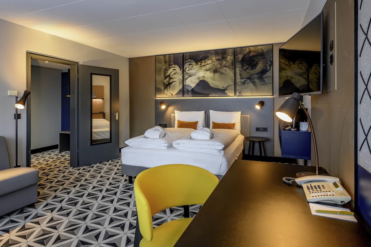 A hotel room with a bed, bedside tables, a desk with a telephone, a chair, and a patterned floor.