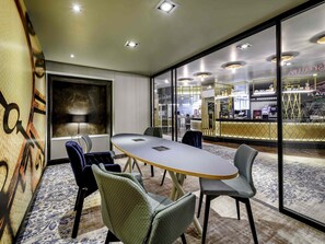 Un salón de conferencias con una gran mesa, sillas y vistas a un área de bar a través de paredes de vidrio.
