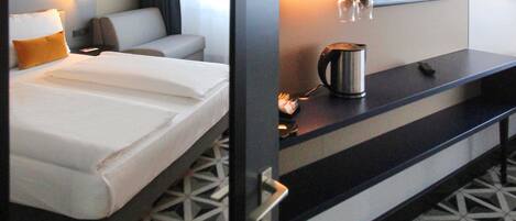A hotel room with a bed, a desk, a coffee maker, and a mirror.