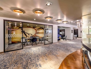 A modern hotel lobby with a glass partition, a seating area with a table and chairs, and a patterned carpet. - Mercure Hotel Freiburg am Munster (Freiburg im Breisgau)