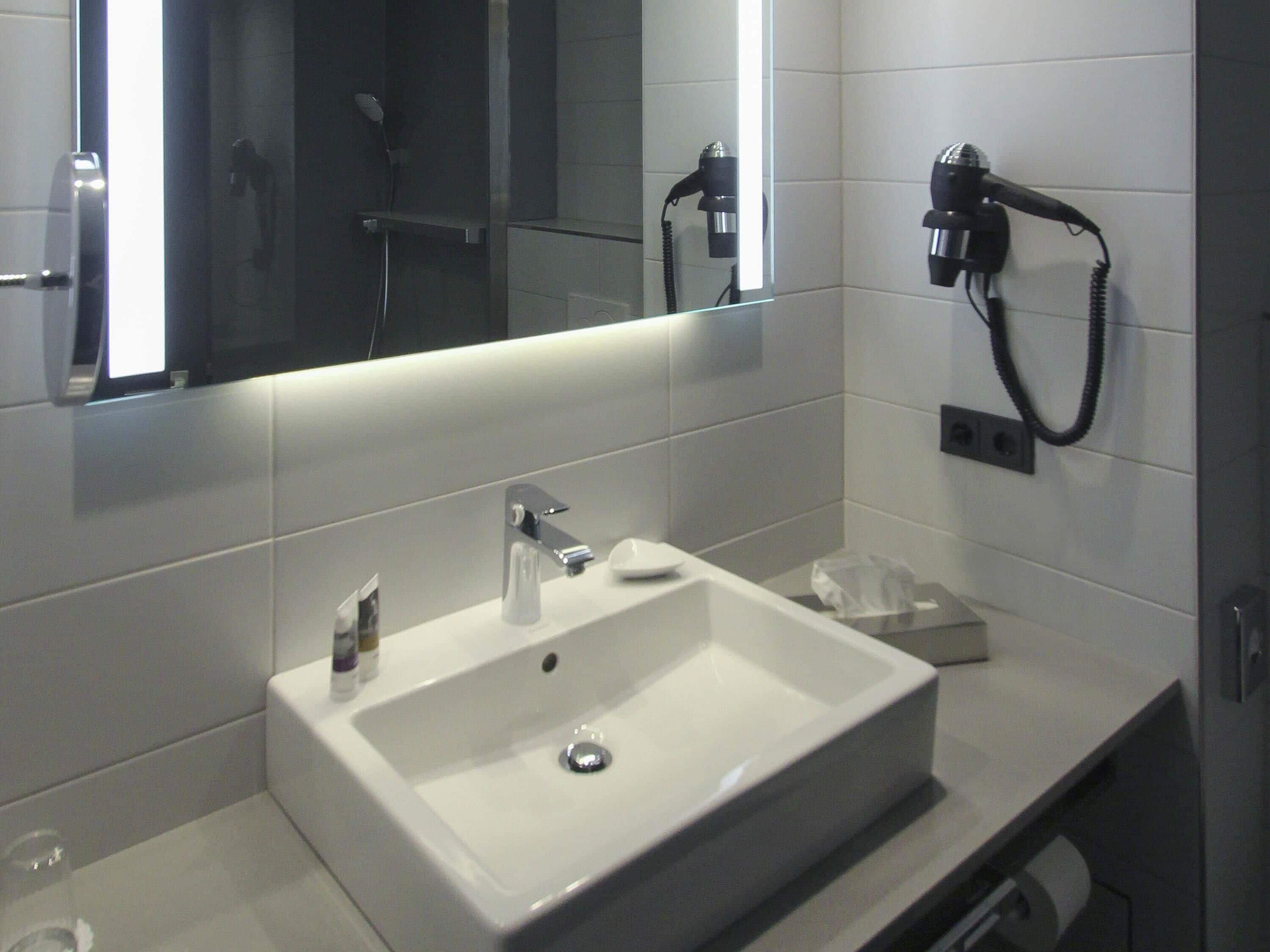 A bathroom with a white sink, a mirror, a hairdryer, and a towel rack.