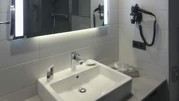 Casa de banho com uma pia branca, espelho, secador de cabelo e porta-toalhas.