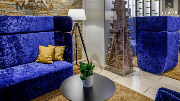 Un moderno vestíbulo de hotel con un sofá azul, una planta en maceta y una escultura de madera original.