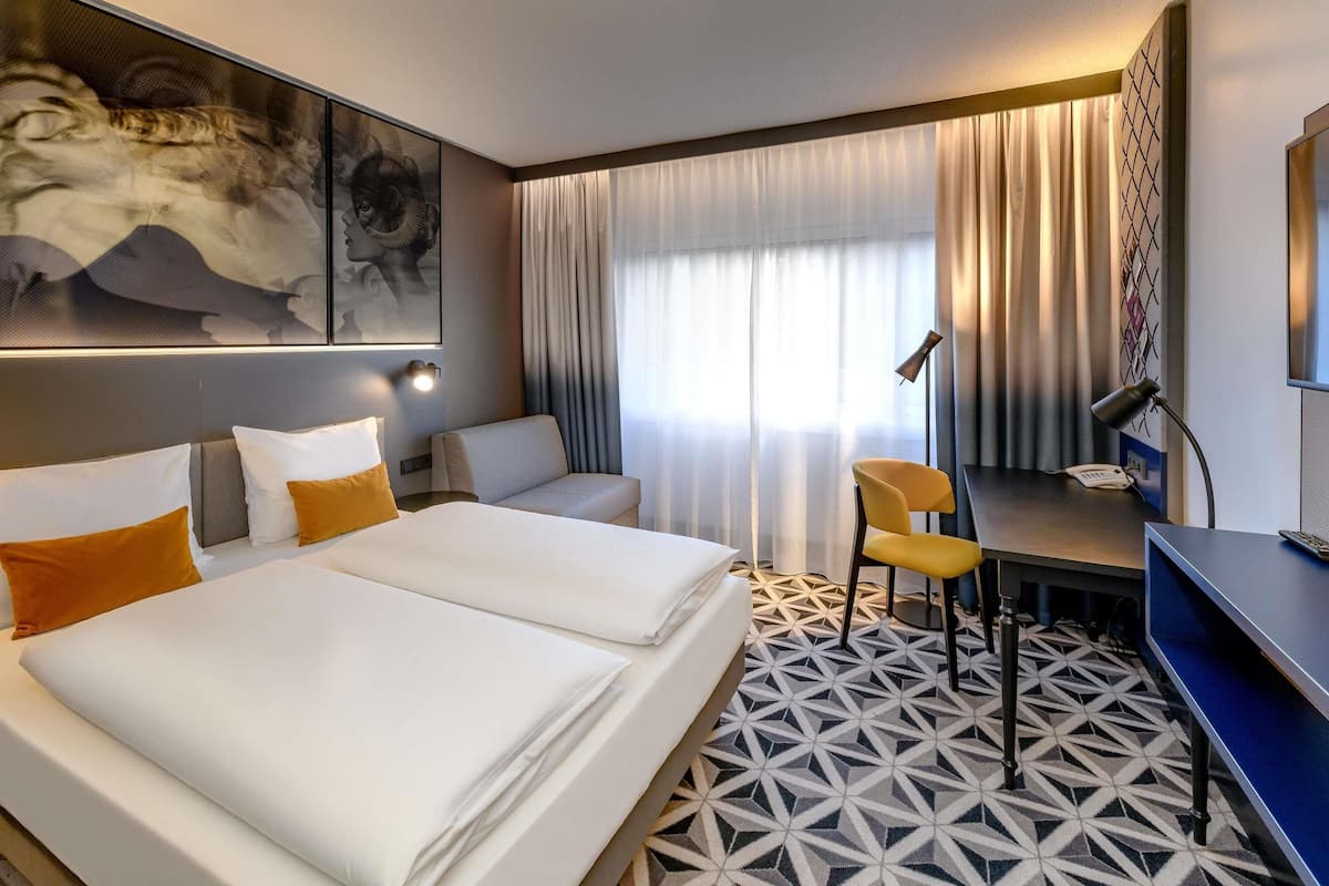 A hotel room with two beds, a desk, a chair, and a large window with curtains.