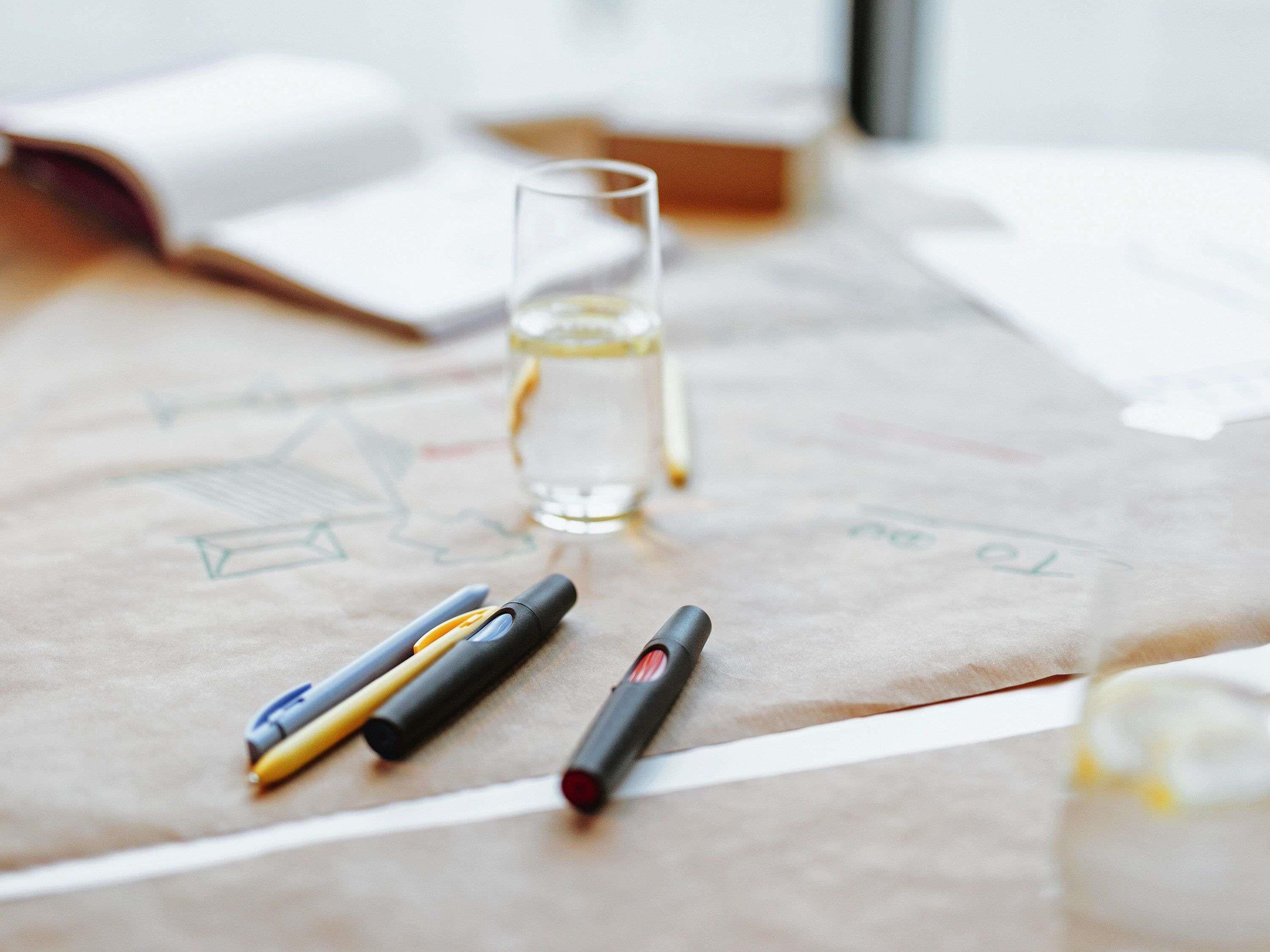 A table with a glass of water, a notebook, and two pens.