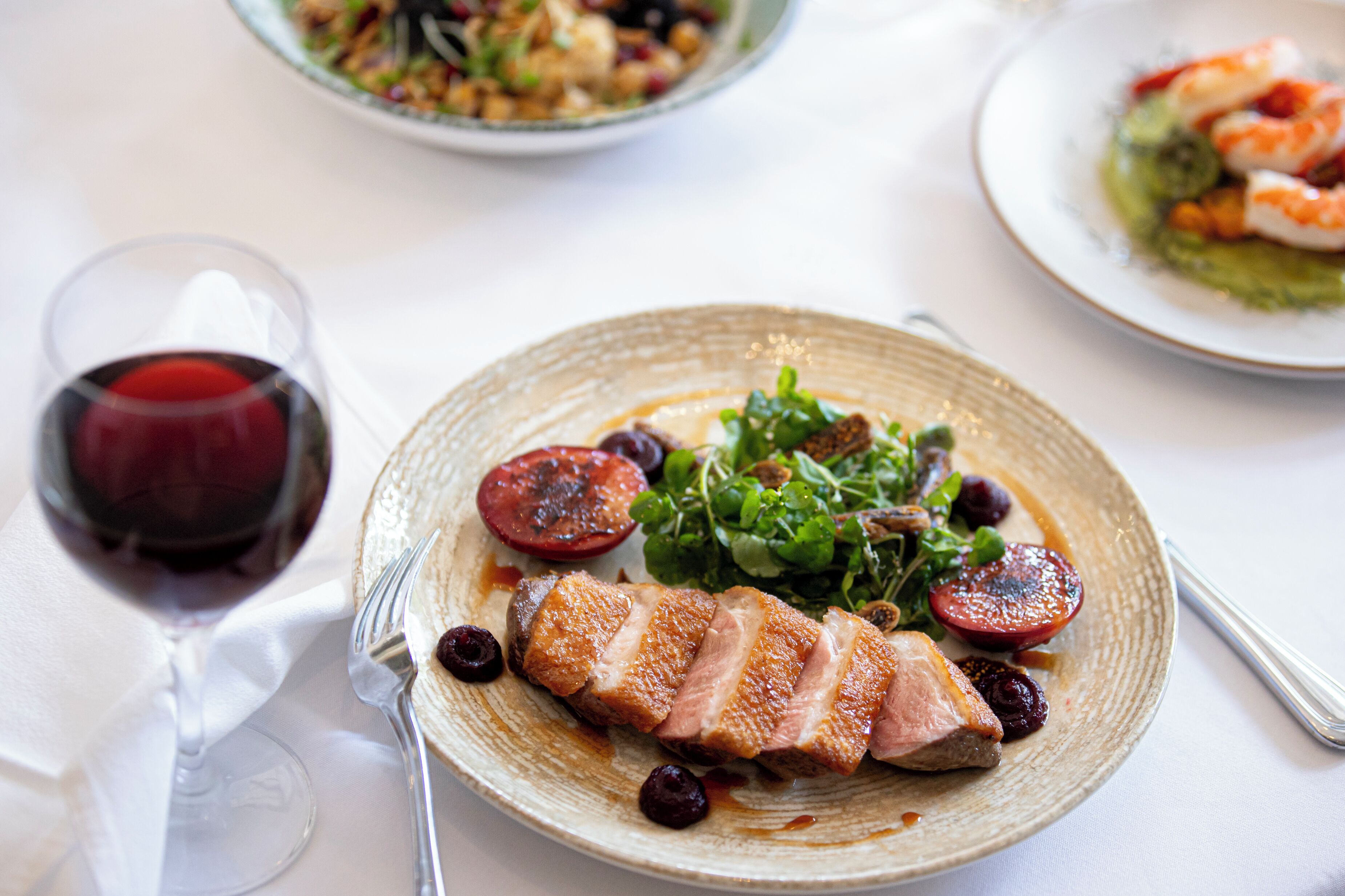 A dining table with a plate of food, a glass of red wine, and a fork.