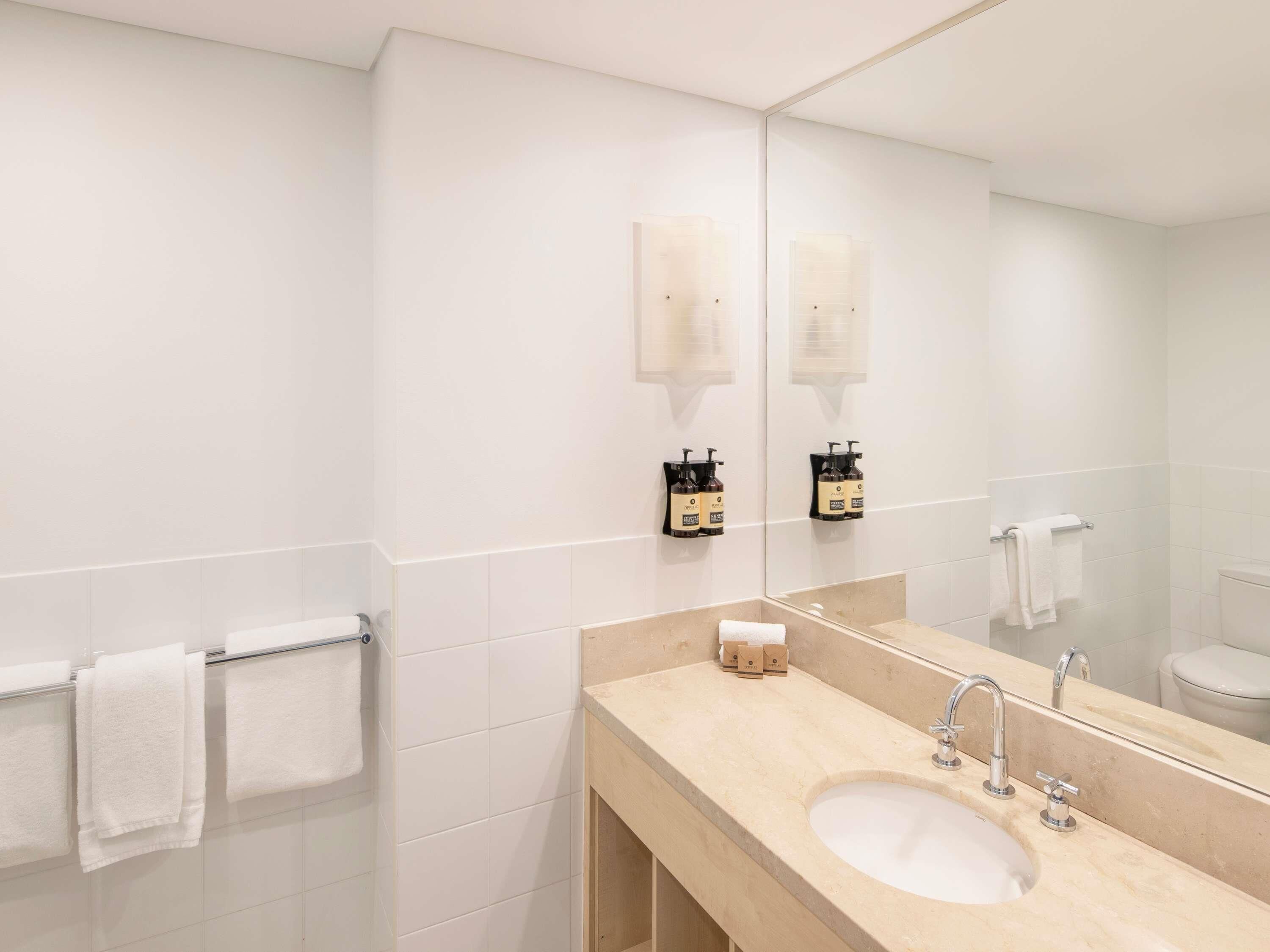 Un baño moderno con un espejo grande, un lavamanos y dos toalleros.