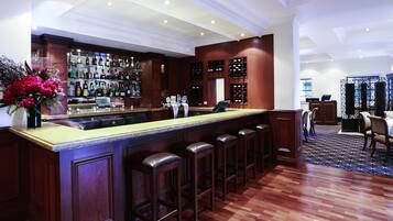 A bar area with a long counter, multiple stools, and a wine rack.