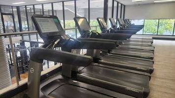 Une rangée de tapis de course dans une salle de sport, avec un écran numérique et un mur recouvert de miroirs.