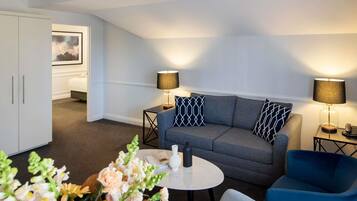 A modern living room with a grey sofa, two side tables with lamps, a white cabinet, and a small round table with a vase of flowers.