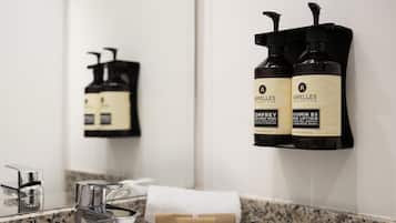 A bathroom with a granite countertop, a mirror, a sink, and two bottles of Apelles body wash on a wall-mounted dispenser.