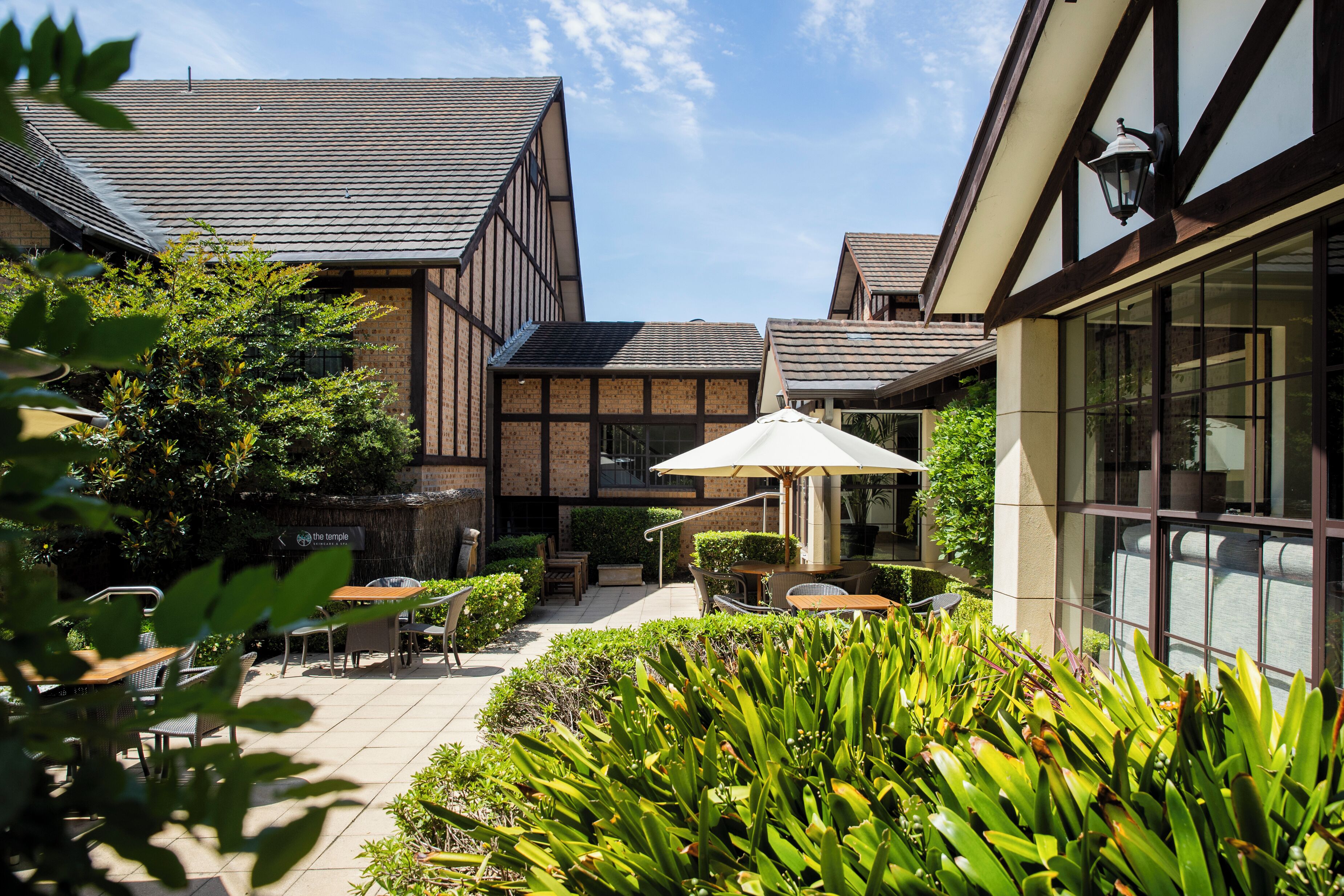 A courtyard with outdoor seating, a pergola, and a building with large windows and a brick facade.