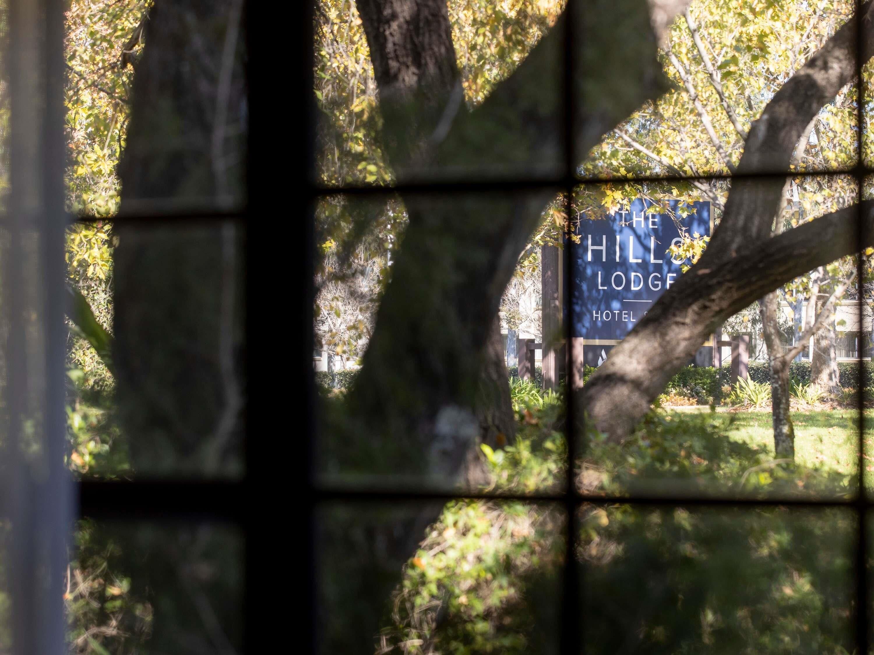 A sign for 'The Hill Lodge Hotel' with a view of trees and a building in the background.
