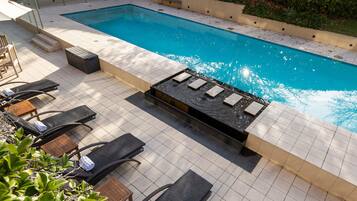 Zona junto a la piscina con sillones de descanso, una pequeña mesa y una chimenea.
